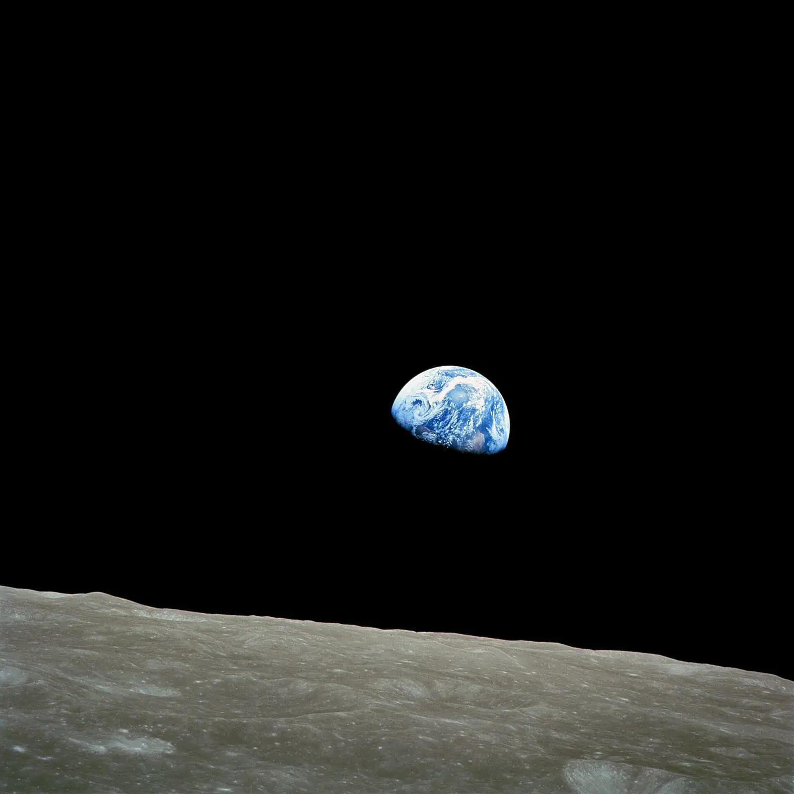 Photographie : la Terre, bleue et blanche, à moitié éclairée, se lève au-dessus de l'horizon gris de la Lune, sur le noir de l'espace.