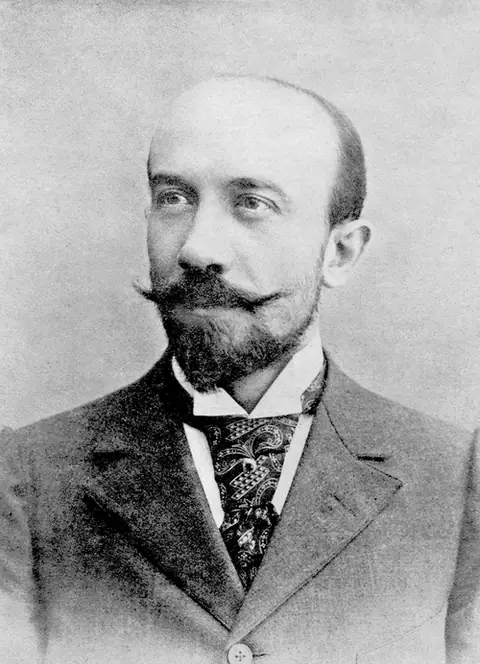 Photographie : Georges Méliès, front dégarni et moustache relevée, en costume et cravate.