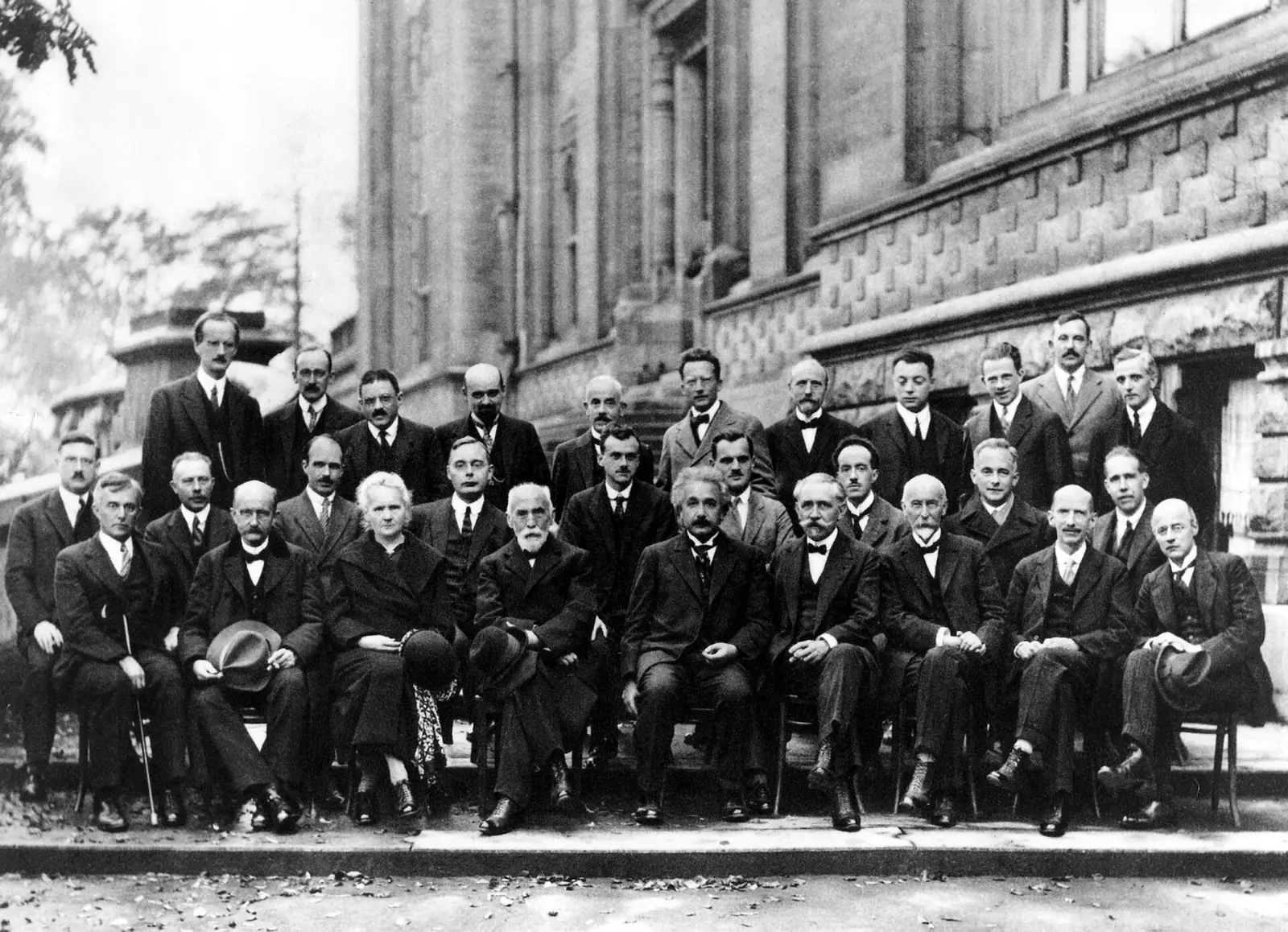 Photographie en noir et blanc : vingt-neuf savants en costume posent sur trois rangs devant un bâtiment ; au premier rang, Marie Curie et Albert Einstein.